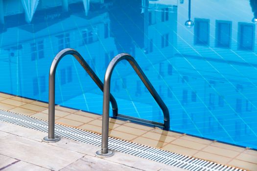 Close up of stair at blue swimming pool with reflection of the hotel.