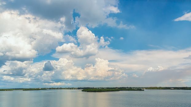 White clouds over a blue sky reflect on the still waters of the lake