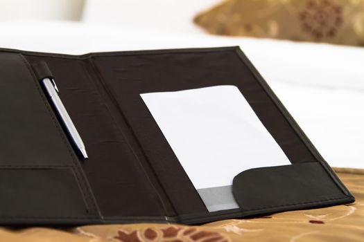 White blank note with pen on bed in hotel room.