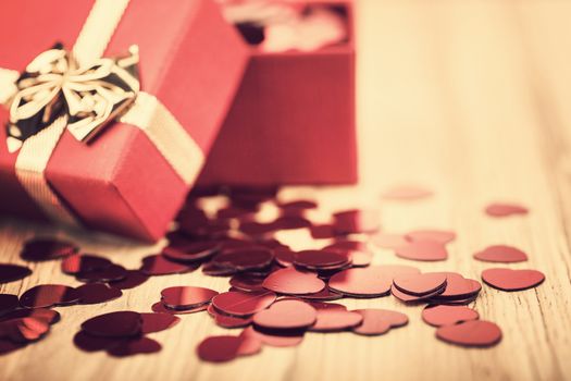 small red hearts confetti and present box on wooden background in retro color