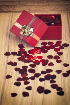 small red hearts confetti and present box on wooden background in retro color tone