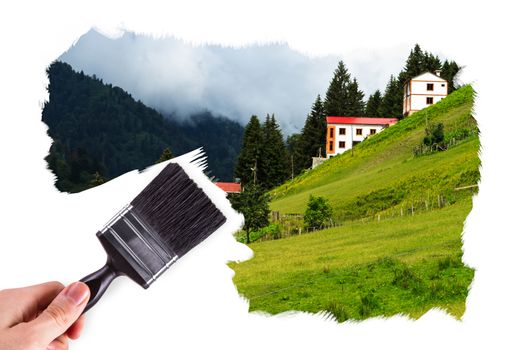 Male hand holding paint brush and painting Ayder Plateau in Rize, Turkey.