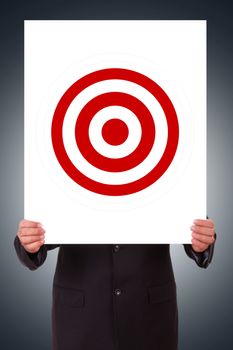 Businessman hand holding white poster with red target on dark background.