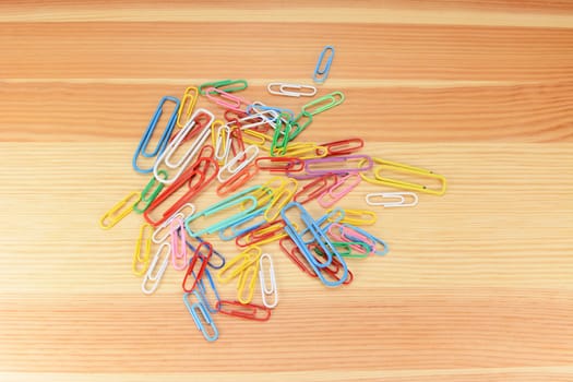 Large and small coloured paper clips on a wooden background