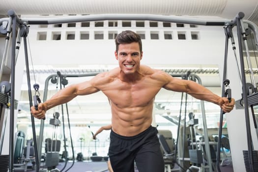 Portrait of a shirtless young muscular man using resistance band in gym