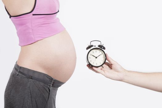hand with alarm clock and tummy of naked pregnant woman