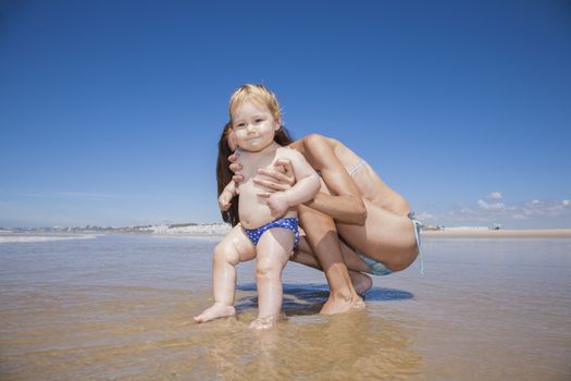 one year baby swimsuit touching water in woman mother hands at beach next to Conil Cadiz Spain
