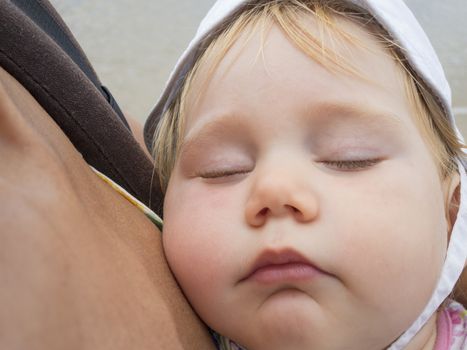 close up face of baby with white hat sleeping in rucksack mom arms