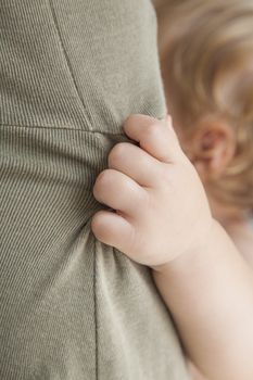 closeup one year blonde baby hand holding green mom dress