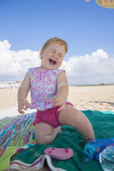 one year happy baby pink shorts laughing squatting over green and stripes towel at beach next to Conil Andalusia Spain