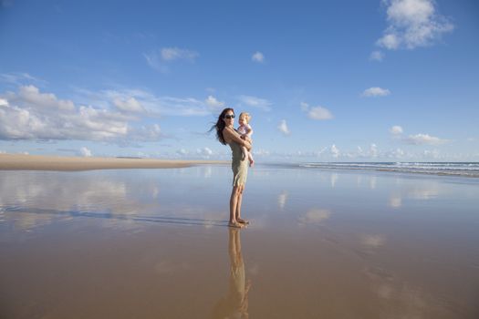 happy green dress woman with sunglasses and one year blonde baby in her arms at beach Conil Cadiz Spain