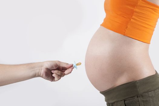 offering pacifier to tummy of naked pregnant woman