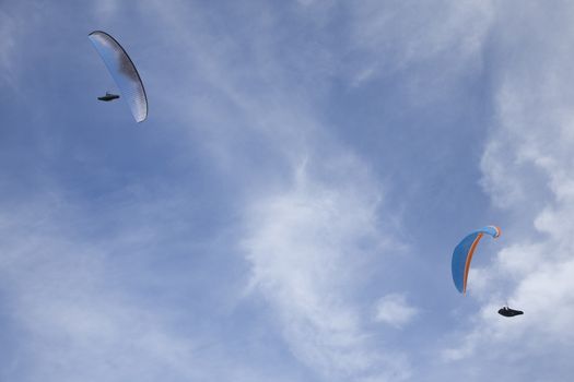 white and blue paragliders flying symmetric in cloudy white and blue sky