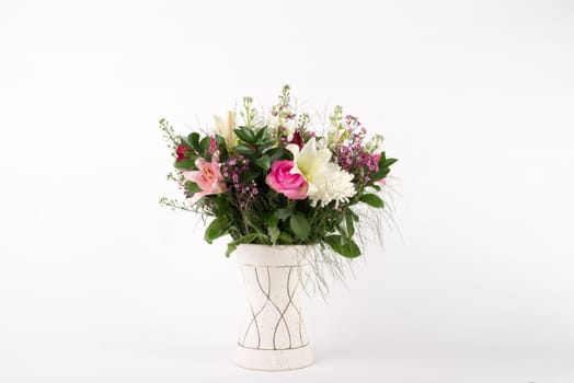 A beautiful flower arrangement in a vase set on a white islolated background.