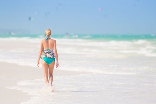 Happy woman having fun, enjoying summer, walking joyfully on tropical beach. Beautiful caucasian model  wearing colorful scarf and turquoise bikini on vacations on Paje beach, Zanzibar, Tanzania