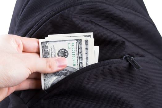 Hand putting dollar banknotes in back pack, isolated on white background.