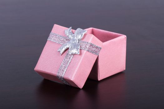 Little, sweet, pink, open gift box with ribbon on wooden table.