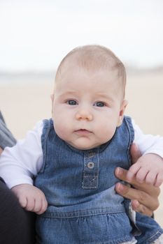 three month baby with jeans dress looking at camera in woman arms outdoor