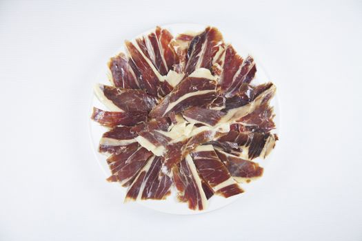 pile of typical spanish iberico ham sliced on white dish