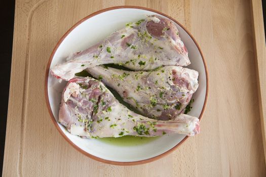 spanish raw legs of baby lamb garlic parsley in white ceramic tray ready to roast