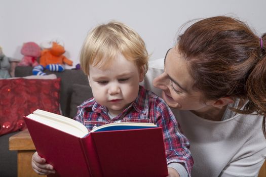 eighteen month aged blonde baby with brunette woman mother reading tale story red book indoor