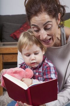 eighteen month aged blonde baby with brunette woman mother reading tale story red book indoor