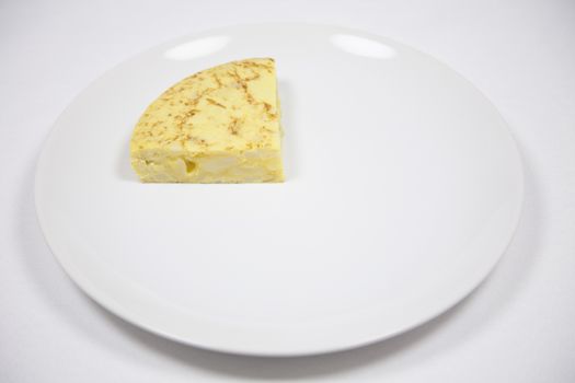 white dish with piece of yellow spanish potato omelette on grey tablecloth