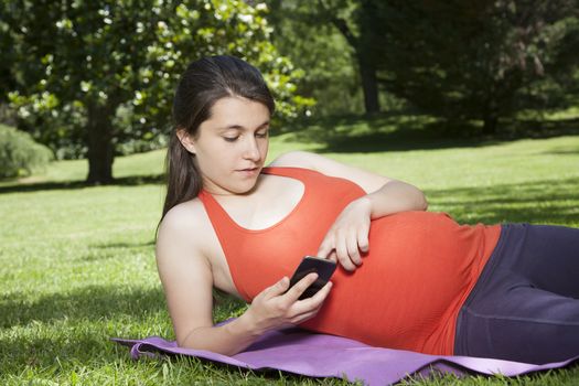 pregnant young woman with orange shirt touching smartphone at a park in Madrid Spain Europe