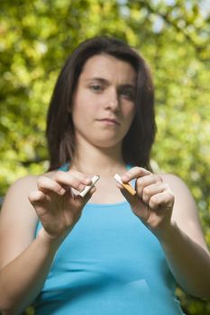 young pregnant woman blue shirt breaking cigarette over green tree background