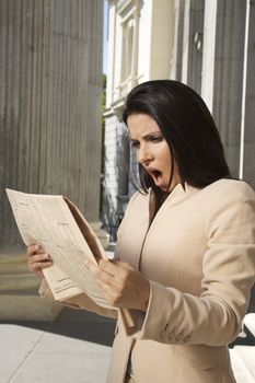portrait of shocked woman reading financial newspaper
