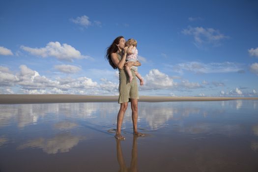 happy green dress woman with sunglasses kiss one year blonde baby in her arms at beach Conil Cadiz Spain