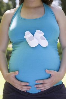 pregnant young woman blue shirt with white small booties on her tummy and green trees background