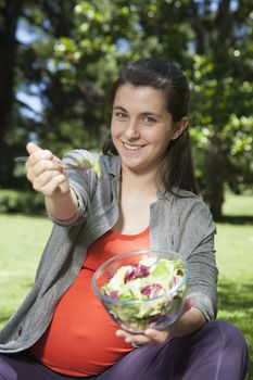 pregnant young woman with orange shirt offering salad sitting at a park in Madrid Spain Europe