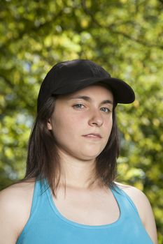 portrait of young pregnant woman with blue shirt black cap threatening face and green trees background