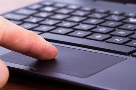 Index finger touching touch pad on laptop keyboard.