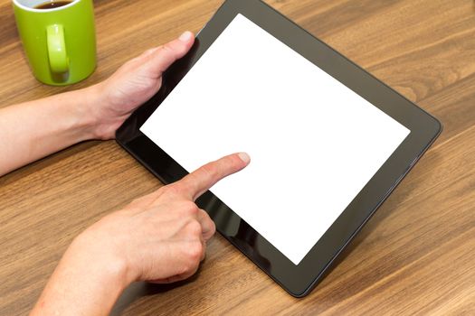 Hand holding and using blank, white screen of tablet on wooden table.