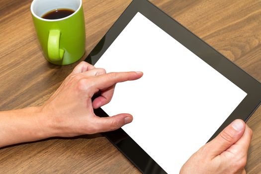 Hand holding and using blank, white screen of tablet on wooden table.