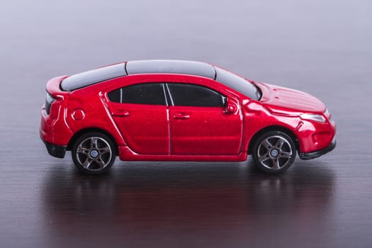 Side view of red, toy, small car on wooden table.