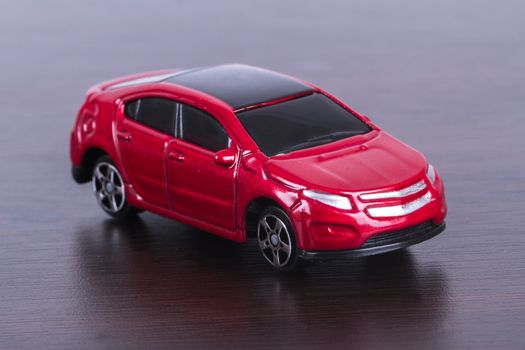 Side view of red, toy, small car on wooden table.