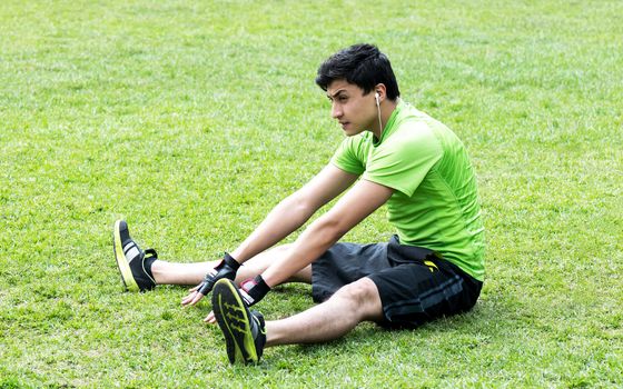 Young man at the park warming and stretching on the grass