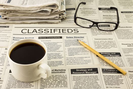 fake classifieds ads on newspaper place on table with glasses, pencil and a cup of coffee