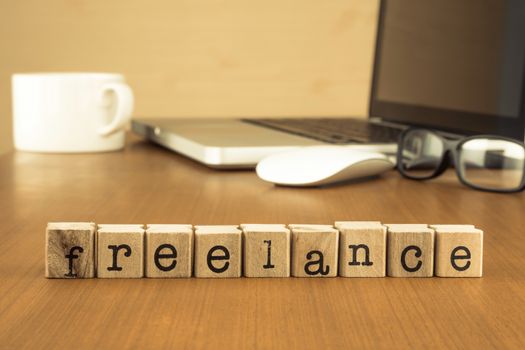 The word freelance on wood stamp stacking on desk with laptop, glasses and a cup of coffee at home office, vintage retro image style