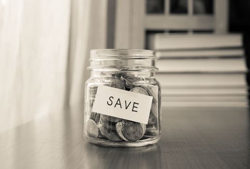 A savings money jar with world coins and save word on label or tag, black and white image