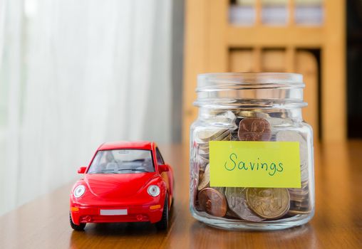 Many world coins in money jar with savings label on jar and a red car model, concept to financial planning for car loan
