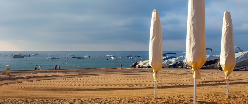 Tossa de Mar, Catalonia, Spain, 2013.06.23 Gran Platja beach in early morning with folded umbrellas and motor boats. Editorial use only