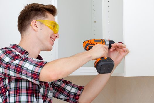 young worker in protective glasses with screwdriver to assemble furniture
