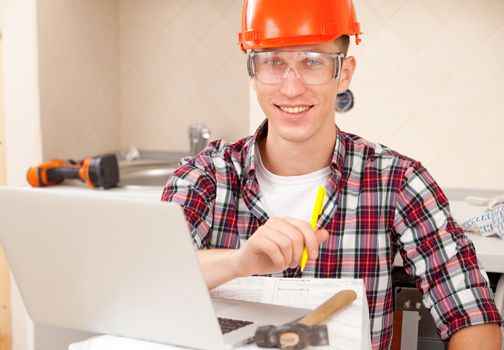 man in protective helmet sits near laptop. repairer receives education in the workplace online