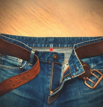 Aged jeans with a leather belt on a wooden surface. Instagram image style