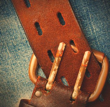 unfastened old leather belt with vintage buckles on the jeans background, instagram image style