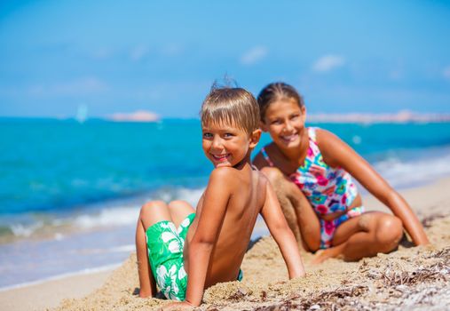 Little boy with his sister relaxing on the sand near ocean